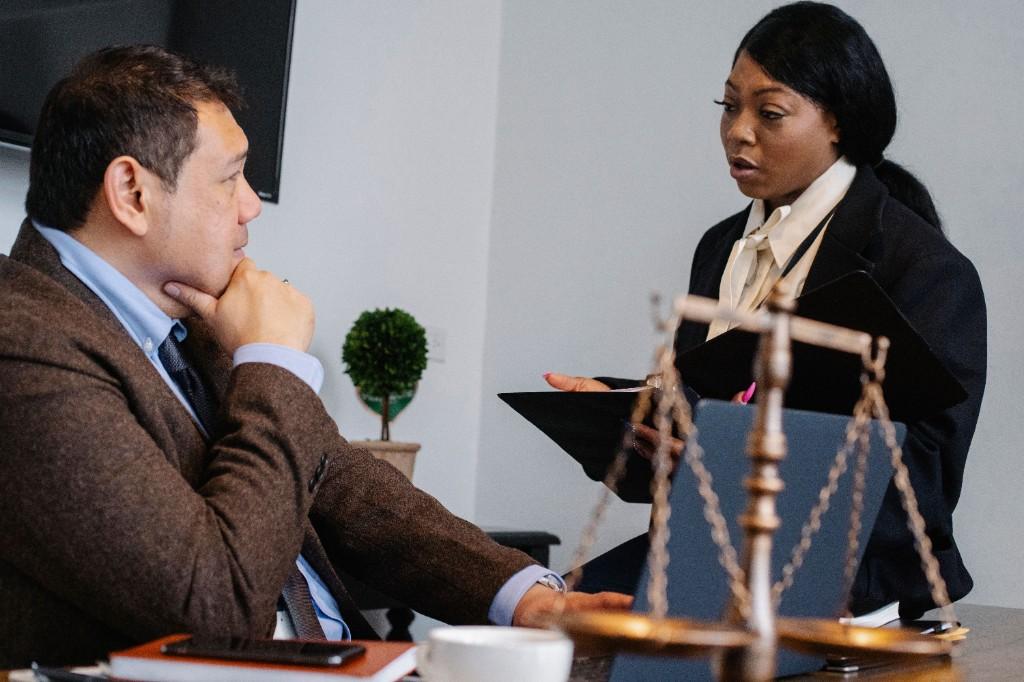 Two legal professionals discussing case materials at a desk with scales of justice in the foreground