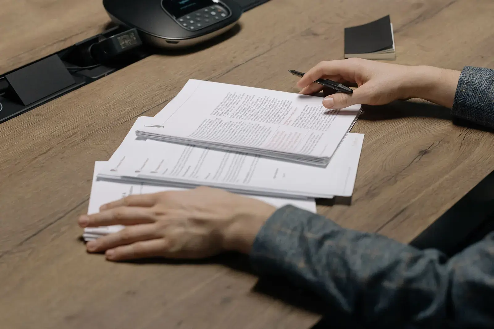 Hands holding a pen over stacks of printed reports on a wooden desk
